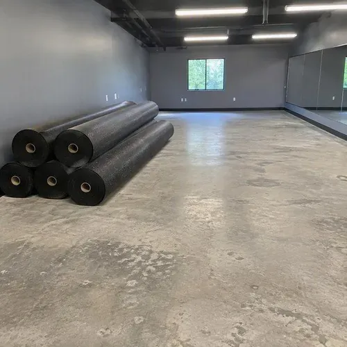 Rolls of black rubber flooring staged on bare gym concrete