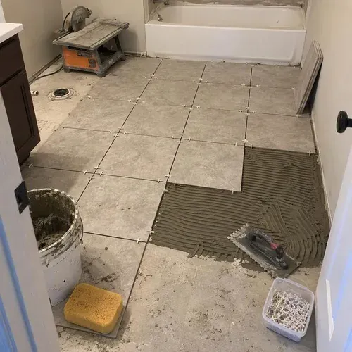 Tile floor half installed with spacers, sponge and bucket